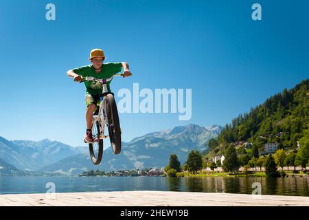 il giovane adolescente maschio salta in alto con la sua bici da terra su una base di lago Foto Stock