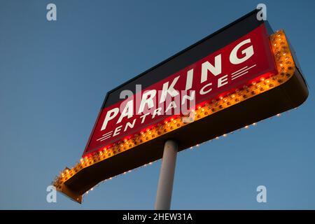 grande cartello rosso illuminato con molte lampade e freccia arancione sul palo con cielo blu Foto Stock