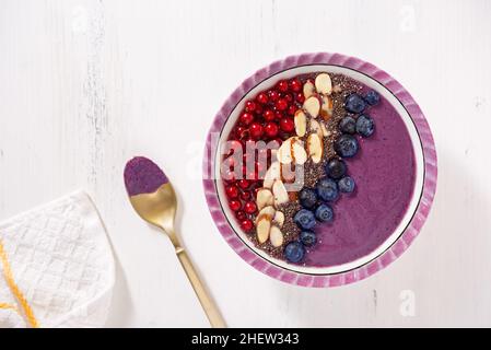 Frullato sano di bacche vegane con mirtilli, ribes rosso, semi di chia e mandorle a fette Foto Stock