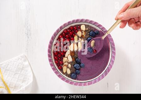 Frullato sano di bacca vegana con mirtilli, ribes rosso, semi di chia e mandorle affettate; mano umana Foto Stock