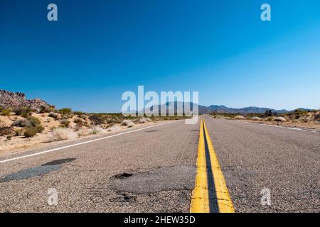 Una strada asfaltica obsoleta con strisce mediali arancioni in corso gettò un deserto negli Stati Uniti Foto Stock