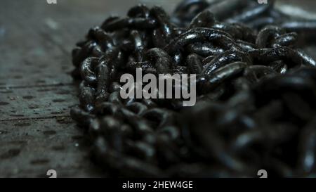 Primo piano per un mucchio di catene metalliche nere che si trovano sul pavimento per lavorare nel settore. Catene in ferro adagiate sul pavimento dell'officina Foto Stock