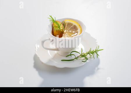 Tè per infusione di zenzero, limone ed erbe servito in una tazza di porcellana bianca. Spazio di copia. Foto Stock