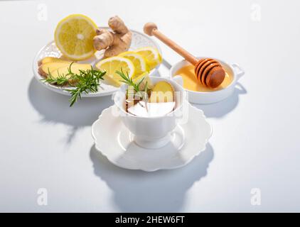 Tè per infusione di zenzero, limone ed erbe servito in una tazza di porcellana bianca. Spazio di copia. Foto Stock