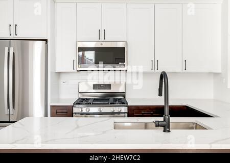 Cucina moderna bianca con rubinetto nero, armadietti in stile Shaker e accessori in acciaio inox Foto Stock