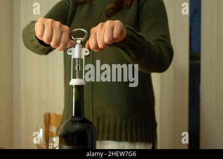 Primo piano su una donna con una giacca verde che stacca una bottiglia di vino rosso su un tavolo Foto Stock