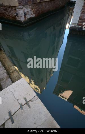 insolito scorcio urbano di venezia. edifici residenziali con intonaco parzialmente rimosso possono essere visti riflessi sulla superficie acquosa di un canale Foto Stock