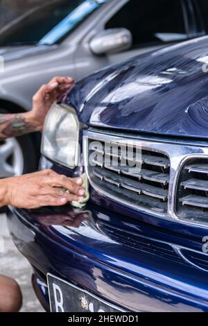 Uomo tatuato lucidare a mano e strofinare un paraurti auto blu con panno per ottenere pulito, lucentezza e dettaglio sul garage. Adatto per lavori di verniciatura e dettagli aut Foto Stock