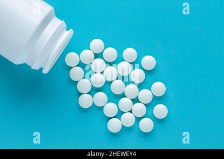 Pillole bianche su sfondo blu, un mazzo di compresse rotonde sparse. Medicamenti in primo piano in bottiglia. Overdose concetto, trattamento della malattia Foto Stock