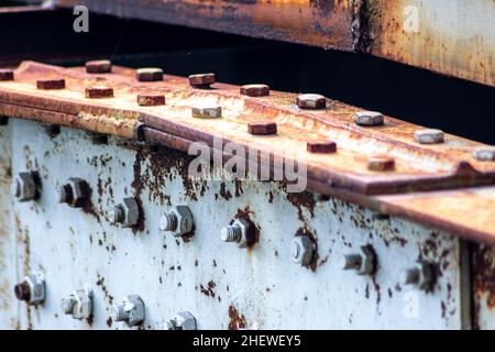 La linea di bulloni e dadi fa una disposizione industriale su grande e pesante ponte di metallo palettando con texture bianco rustico in cantiere Foto Stock