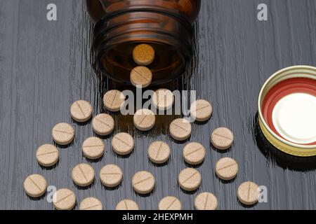 pillole mediche e bottiglia di vetro marrone su tavolo di legno nero Foto Stock