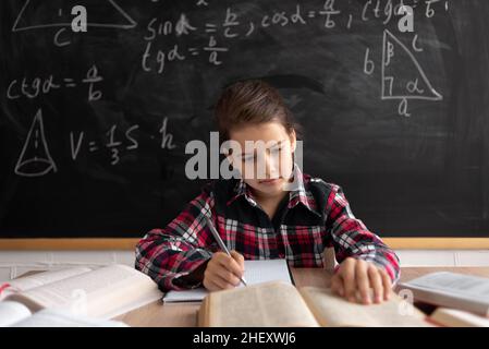 Ritorno a scuola e happy time. Studentessa o studentessa che studia in aula sullo sfondo della lavagna. La ragazza caucasica legge un libro e ma Foto Stock