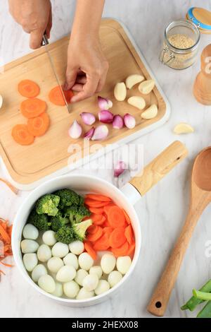 Cucina - le mani dello chef preparano brodo di pollo (brodo o bouillon) con verdure in una pentola. Cucina - grigio cemento piano di lavoro scenario dall'alto (top v Foto Stock