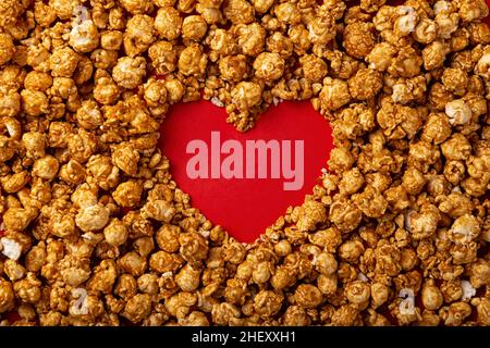 immagine del concetto di amore della cornice a forma di cuore fatta di popcorn caramello su sfondo rosso Foto Stock