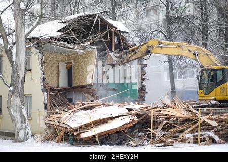 Demolizione di edifici. L'escavatore rompe la vecchia casa a due piani. Paesaggio urbano industriale con processo di distruzione. Foto Stock