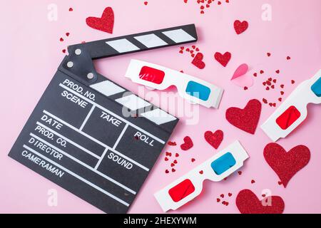 Concetto di notte del film del giorno di San Valentino. Popcorn, 3D bicchieri bordo clapper su sfondo rosa. Accoglienti piani di vacanza per gli amanti Foto Stock