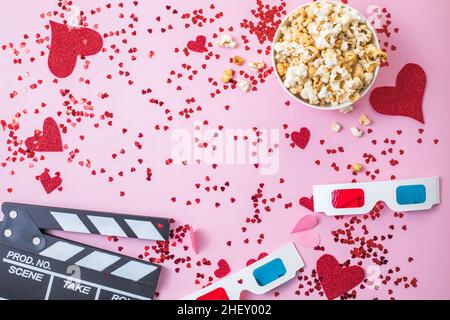 Concetto di notte del film del giorno di San Valentino. Popcorn, 3D bicchieri bordo clapper su sfondo rosa. Accoglienti piani di vacanza per gli amanti Foto Stock