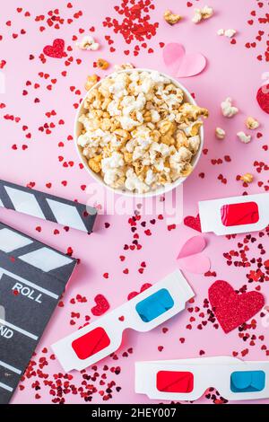 Concetto di notte del film del giorno di San Valentino. Popcorn, 3D bicchieri bordo clapper su sfondo rosa. Accoglienti piani di vacanza per gli amanti Foto Stock