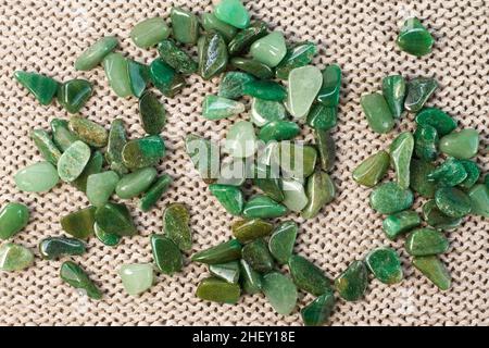 Macrofooting di pietra minerale naturale esemplare - pietra d'aventurina verde tumbled su sfondo beige vista dall'alto Foto Stock