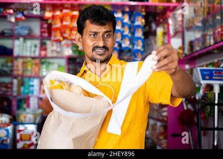 Cliente scioccato a Kirana o negozio di alimentari dopo aver visto la ricezione di fatture alimentari - concetto di inflazione, aumento dei prezzi e consumismo. Foto Stock