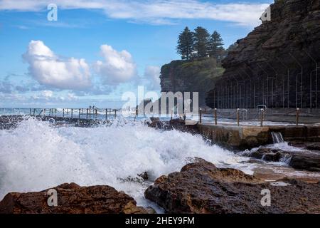 Surfer naviga grandi onde a Avalon Beach per entrare nell'oceano per il surf, grandi onde si infrangono sulla piscina Rockpool, Sydney, Australia Foto Stock