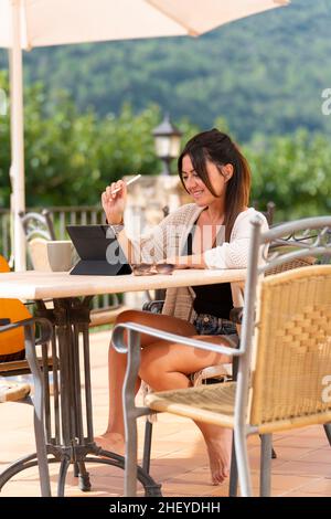 Donna seduta su una terrazza scrivendo su un tablet con penna digitale Foto Stock