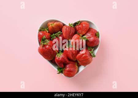 Deliziosa fragola organica brutta matura in piatto a forma di cuore isolato su sfondo rosa. Vista dall'alto. Prodotti ecologici biologici. Foto Stock