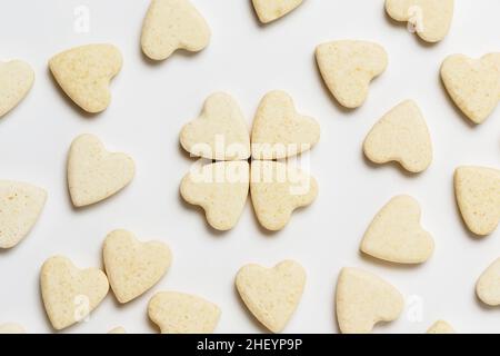 San Valentino biglietto di auguri minimalistico, dolci biscotti a forma di cuore sparsi su sfondo bianco, piatto Foto Stock