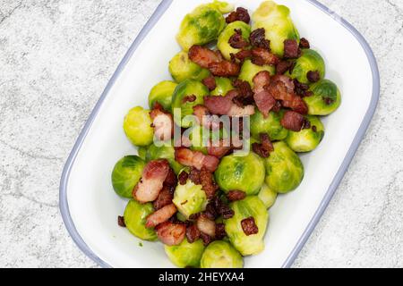 Bruxelles germogli con pancetta lardons in un piatto tradizionale smalto. Su sfondo concreto Foto Stock