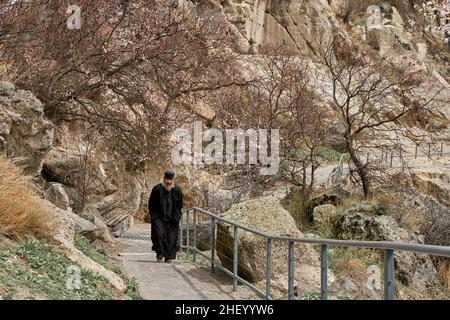 Il prete Ruzin in una cassoneta cammina attraverso la città grotta nella roccia. Akhaltsikhe, Georgia - 04.09.2021 Foto Stock