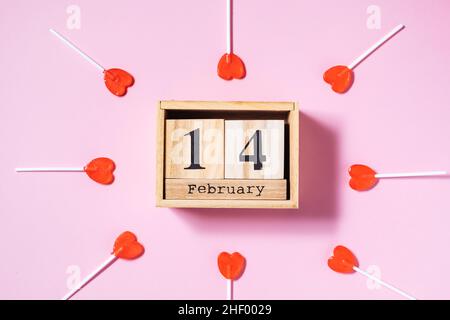 Torta al cioccolato a forma di cuore su un piatto giallo con praline al cioccolato a forma di cuore su sfondo viola con due nastri rossi. San Valentino Foto Stock