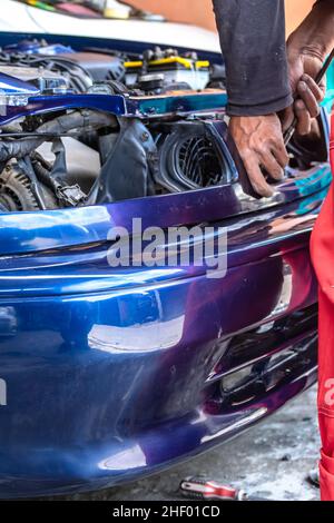meccanico uomo che fissa e ripara l'automobile blu con le parti non montate al garage auto Foto Stock
