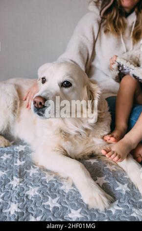 Mamma e figlia coccolano comodamente a casa con il loro animale domestico Labrador Retriever Foto Stock
