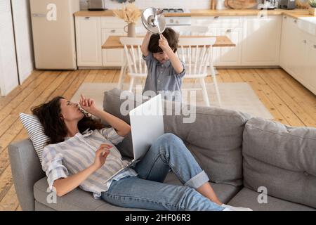 La mamma sopraffatta chiede al figlio di navigare in Internet in silenzio per lavoro. Genitore e bambino su blocco covid Foto Stock