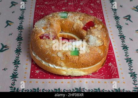 Una torta di forma ovale con ripieno dolce con panna montata dolce decorata con mandorle e canditi su una tovaglia con decorazioni natalizie. Foto Stock