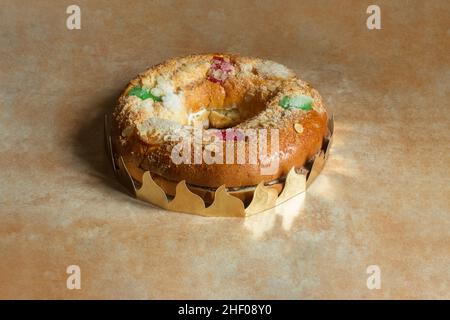 Grande torta di ciambelle piena di panna montata dolce e meringa con frutta candita, mandorle, zucchero, circondata da una corona su un disegno testurizzato astratto Foto Stock