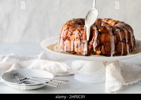 Pane di scimmia alla cannella di mele su un piedistallo con la glassa che viene gocciolato sulla parte superiore Foto Stock