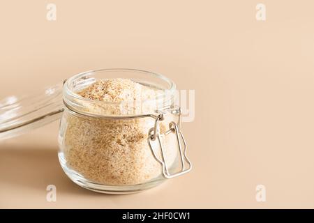Buccia di psyllium in vaso di vetro supplemento di fibra solubile per l'intestino su sfondo beige. Superfood per sano, abbassa il colesterolo, bilancia il sangue su Foto Stock
