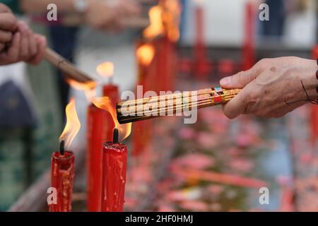 primo piano la mano che brucia incenso bastoni sul fuoco rosso della candela nel tempio. Concetto di cultura buddhista asiatica Foto Stock