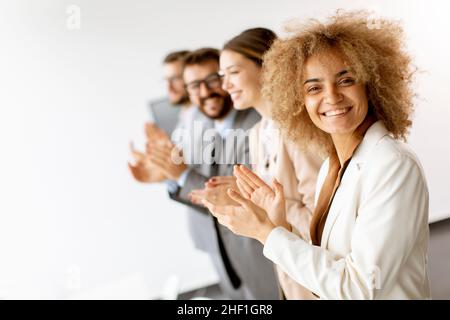 Gruppo di giovani collaboratori diversi in fila e applauditi in ufficio Foto Stock