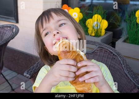 Il bambino affamato mangia appetitosamente croissant fresco Foto Stock