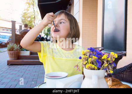 Una ragazza sta gustando tè alla frutta e un croissant fresco per la prima colazione in una caffetteria. Foto Stock