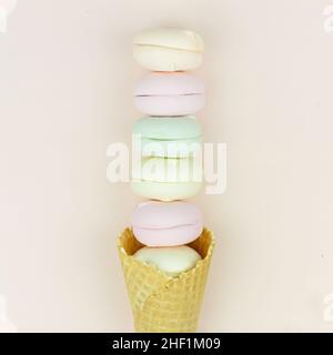 Il cono di cialda giallo con le marshmallow verdi, rosa e gialle assomiglia ai amaretti su sfondo pastello Foto Stock