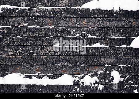 Parte del muro di legno di una casa bruciata coperta di neve. Struttura di legno bruciato Foto Stock