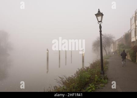 Un uomo fa una passeggiata di mattina presto in mezzo alla fitta nebbia sulle rive del Tamigi a Strand-on-the-Green, Chiswick, Londra, Inghilterra, Regno Unito Foto Stock