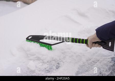 Rimozione della neve, auto nella neve. La donna pulisce l'auto dalla neve. Foto Stock