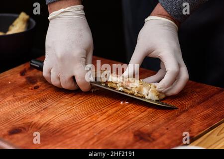 L'uomo taglia il pesce fritto, processo di cottura della zuppa Suquet de Peix con patate Foto Stock