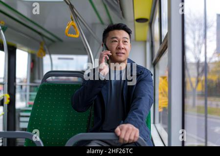 Uomo asiatico ansioso e spaventato, a bordo di un autobus pubblico, un passeggero che parla su un telefono cellulare Foto Stock