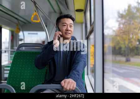 uomo asiatico in autobus pubblico passeggeri divertirsi a parlare sul telefono cellulare, in abiti casual Foto Stock