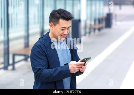 Allegro e felice asiatico usando il telefono sorridente e guardando la macchina fotografica, vicino aeroporto, uomo d'affari in viaggio turistico Foto Stock